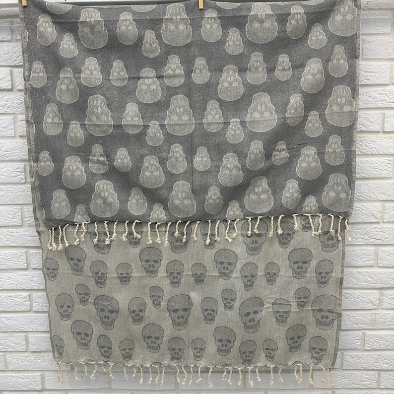 May include: Gray and white cotton throw blanket with a skull pattern. The blanket has fringe on the bottom edge.