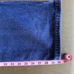 May include: Close-up of blue denim fabric with a pink measuring tape showing a length of 30 inches. The denim has a textured appearance and is likely part of a pair of jeans.