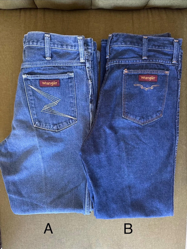 May include: Two pairs of blue denim Wrangler jeans. One pair features a zig-zag design on the back pocket, while the other has a simple pocket design. Both pairs have the Wrangler logo on the back pocket.