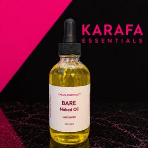May include: A clear glass dropper bottle filled with yellow oil, featuring a white label that reads KARAFA ESSENTIALS, BARE Naked Oil, UNSCENTED, and 4OZ/120ML. The bottle has a black dropper cap and is positioned against a black and pink background.