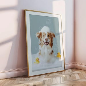 May include: Framed print featuring a happy dog in a bubble bath with two yellow rubber duckies. The dog has brown and white fur and is surrounded by bubbles. The frame is gold.