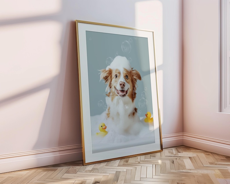May include: Framed print featuring a happy dog in a bubble bath with two yellow rubber duckies. The dog has brown and white fur and is surrounded by bubbles. The frame is gold.
