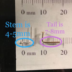 May include: Two nose studs are shown against a ruler. One is silver with a 4-5 mm stem, and the other is gold with a 7-8 mm tail. The image includes text indicating the measurements of each stud.