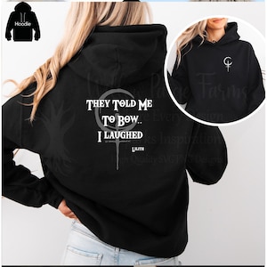 May include: Black hoodie with white text on the back that reads "THEY TOLD ME TO BOW.. I LAUGHED" and a cross-like symbol. The front of the hoodie has a small white symbol. The hoodie has a hood and long sleeves.