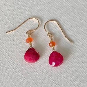 Peut inclure: Une paire de boucles d'oreilles en or avec une pierre rouge en forme de larme et une petite pierre orange sur chaque boucle d'oreille.