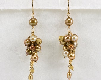 May include: A pair of gold dangle earrings with a cluster of brown and cream pearls. The earrings have a delicate chain design with small gold beads.