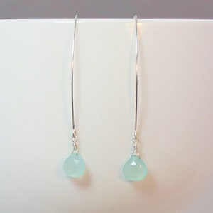 Pode incluir: Um par de brincos pendurados elegantes. Cada brinco apresenta um fio longo e fino de prata com uma pequena pedra preciosa em forma de l&aacute;grima azul clara na parte inferior. As pedras preciosas t&ecirc;m uma superf&iacute;cie facetada, que capta a luz.