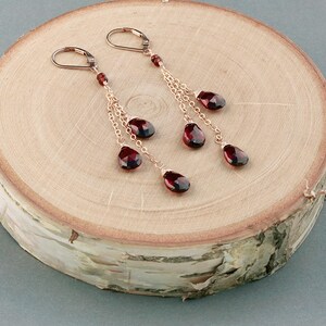 May include: A pair of dangle earrings with multiple strands of gold chain and red gemstone drops.