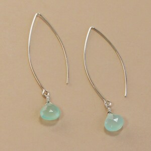 Pode incluir: Um par de brincos pendurados prateados. Cada brinco apresenta um design de fio curvo e alongado com uma pequena pedra preciosa verde-claro facetada em forma de gota pendurada na parte inferior. As pedras preciosas s&atilde;o de uma cor verde pastel suave.
