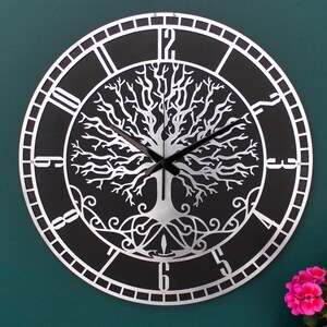 May include: A round, decorative wall clock with a black face and silver-colored metal frame. The clock features a tree of life design in the center and Roman numeral hour markers. The clock hands are black.
