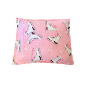 Puede incluir: Una almohada rectangular rosa con un estampado de patines de hielo blancos con cordones rosas y peque&ntilde;os dise&ntilde;os de copos de nieve. La almohada tiene un borde rosa y est&aacute; sobre un fondo blanco.