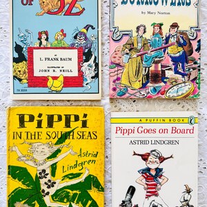 Puede incluir: Cuatro libros infantiles antiguos con portadas ilustradas: Ozma of Oz de L. Frank Baum, The Borrowers de Mary Norton, Pippi in the South Seas de Astrid Lindgren y Pippi Goes on Board de Astrid Lindgren, dispuestos en una cuadr&iacute;cula.