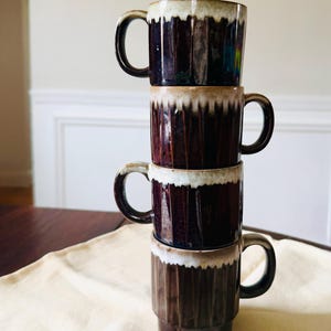 May include: A stack of four ceramic mugs. The mugs are dark brown with vertical ribbed detailing and a white, textured rim. Each mug has a dark brown handle. The mugs are stacked on top of each other.