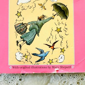 Puede incluir: Una portada de libro con borde rosa y panel central amarillo. Una ilustraci&oacute;n muestra a una figura con abrigo y sombrero volando con un paraguas negro y un bolso estampado, rodeada de estrellas amarillas, nubes blancas y dos p&aacute;jaros. El texto dice: With original illustrations by Mary Shepard.