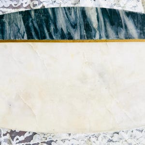 May include: Rectangular marble serving board with a white base and a dark green and gray marbled top section. A thin gold band separates the two sections. The board is set on a white lace cloth.