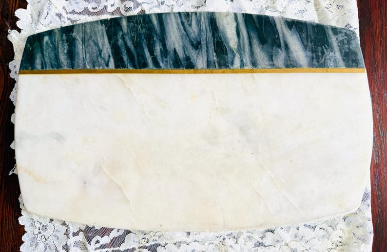 May include: Rectangular marble serving board with a white base and a dark green and gray marbled top section. A thin gold band separates the two sections. The board is set on a white lace cloth.
