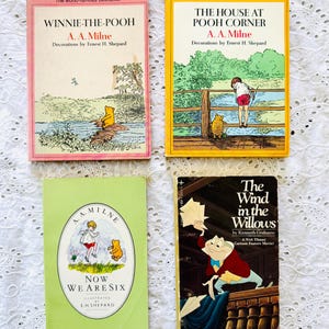 Puede incluir: Cuatro libros de bolsillo antiguos que incluyen Winnie-the-Pooh con portada rosa, The House at Pooh Corner con portada amarilla, Now We Are Six con portada verde claro y The Wind in the Willows con portada oscura y un personaje de rana.