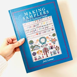 May include: A blue book titled "MAKING SAMPLERS" with "New & Traditional Designs" text. The cover features a sampler design with letters, numbers, and floral motifs. The author's name, Jutta Lammer, is at the bottom.