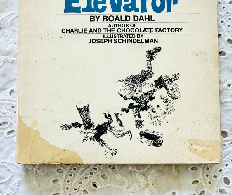 Puede incluir: Un libro de tapa dura vintage titulado Charlie and the Great Glass Elevator de Roald Dahl. La cubierta de color blanco hueso presenta ilustraciones en tinta negra de dos figuras en movimiento, con el autor Roald Dahl y el ilustrador Joseph Schindelman.