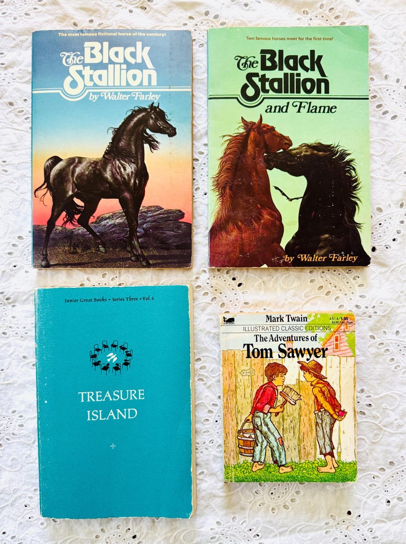 Puede incluir: Cuatro libros antiguos que incluyen The Black Stallion y The Black Stallion and Flame de Walter Farley, Treasure Island de Junior Great Books Series Three Vol. 6, y The Adventures of Tom Sawyer de Mark Twain con una ilustraci&oacute;n en la portada.