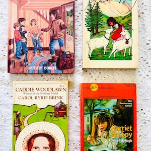 Puede incluir: Cuatro libros de bolsillo infantiles titulados Ida Early Comes Over the Mountain, Heidi, Caddie Woodlawn y Harriet the Spy. Cada portada presenta ilustraciones coloridas de personajes y escenas, con los nombres de los autores visibles.