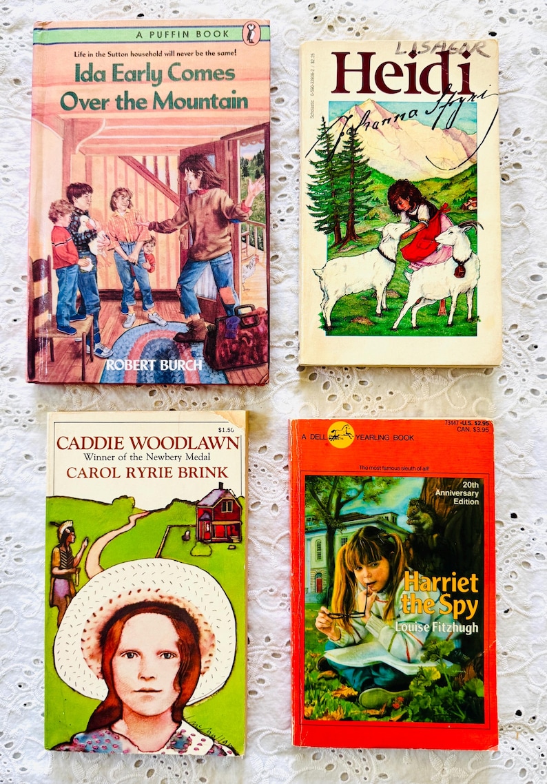 Puede incluir: Cuatro libros de bolsillo infantiles titulados Ida Early Comes Over the Mountain, Heidi, Caddie Woodlawn y Harriet the Spy. Cada portada presenta ilustraciones coloridas de personajes y escenas, con los nombres de los autores visibles.