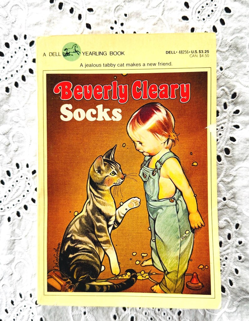 May include: A paperback book titled Socks by Beverly Cleary, published by Dell Yearling. The cover features a brown tabby cat facing a young child wearing green overalls. The text reads A Dell Yearling Book, A jealous tabby cat makes a new friend.