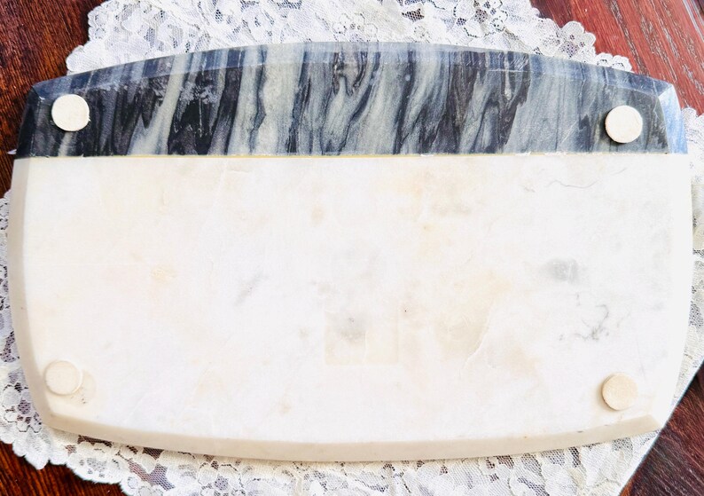 May include: Rectangular marble serving tray with a white base and a gray and black marbled top section. The tray has four small, round feet and is set on a white lace doily.