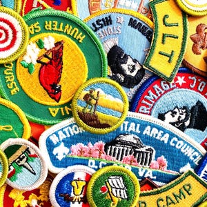 May include: A collection of colorful embroidered patches with various designs and text. Patches include images of a cardinal, a hiker, and the text "JLT" and "NATIONAL CAPITAL AREA COUNCIL". The patches are in various shapes and sizes.
