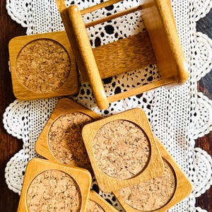 May include: Wooden coasters with cork inserts and a small wooden chair are arranged on a white lace doily. The coasters have a square wooden frame and a circular cork center. The chair is made of the same light-colored wood.