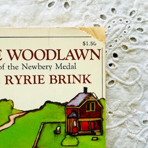 Puede incluir: Una portada de libro con el texto CADDIE WOODLAWN, of the Newbery Medal, y CAROL RYRIE BRINK. La portada muestra una casa roja con techo oscuro sobre un paisaje verde con un camino. En la esquina superior derecha se ve el precio de 1,50 $.