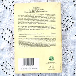 May include: The back cover of the paperback book Socks by Beverly Cleary, illustrated by Beatrice Darwin. It features a light yellow background with black text, a barcode, a small green horse logo, and publishing details for A Yearling Book.