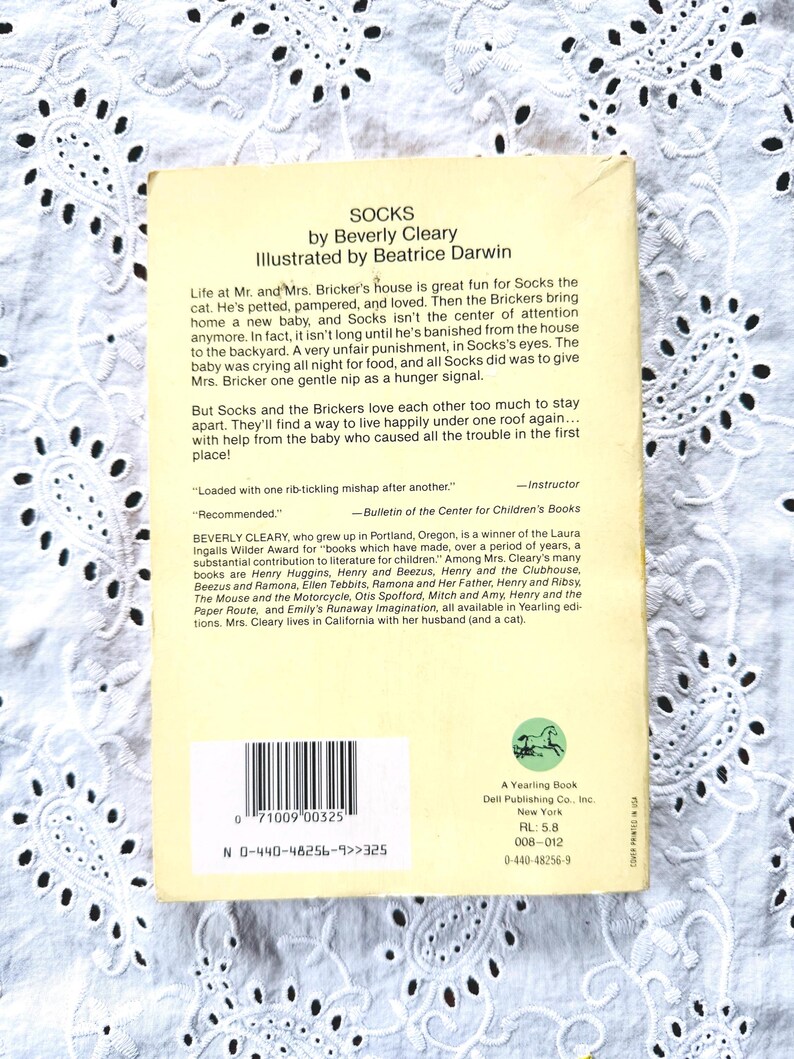 May include: The back cover of the paperback book Socks by Beverly Cleary, illustrated by Beatrice Darwin. It features a light yellow background with black text, a barcode, a small green horse logo, and publishing details for A Yearling Book.