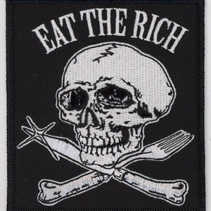 May include: Black and white embroidered patch with a skull and crossbones design. The skull has a fork and a bone for crossbones. The text "EAT THE RICH" is above the skull.