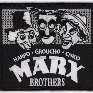 May include: Black and white embroidered patch featuring the Marx Brothers. The patch shows the faces of Harpo, Groucho, and Chico with the text "HARPO - GROUCHO - CHICO" and "MARX BROTHERS" in white.