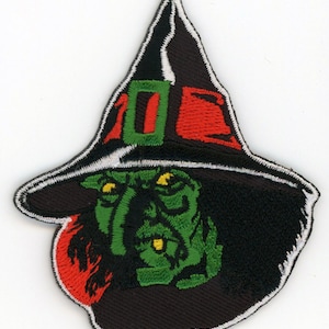 May include: Green witch face with a black pointed hat with a red and green band. The witch has yellow eyes and a green face.