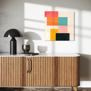 Puede incluir: Una impresi&oacute;n de arte abstracto moderno con formas geom&eacute;tricas en rosa, naranja, amarillo, turquesa y negro sobre un fondo crema. La impresi&oacute;n est&aacute; colgada en una pared blanca sobre un gabinete de madera con una tapa de m&aacute;rmol.