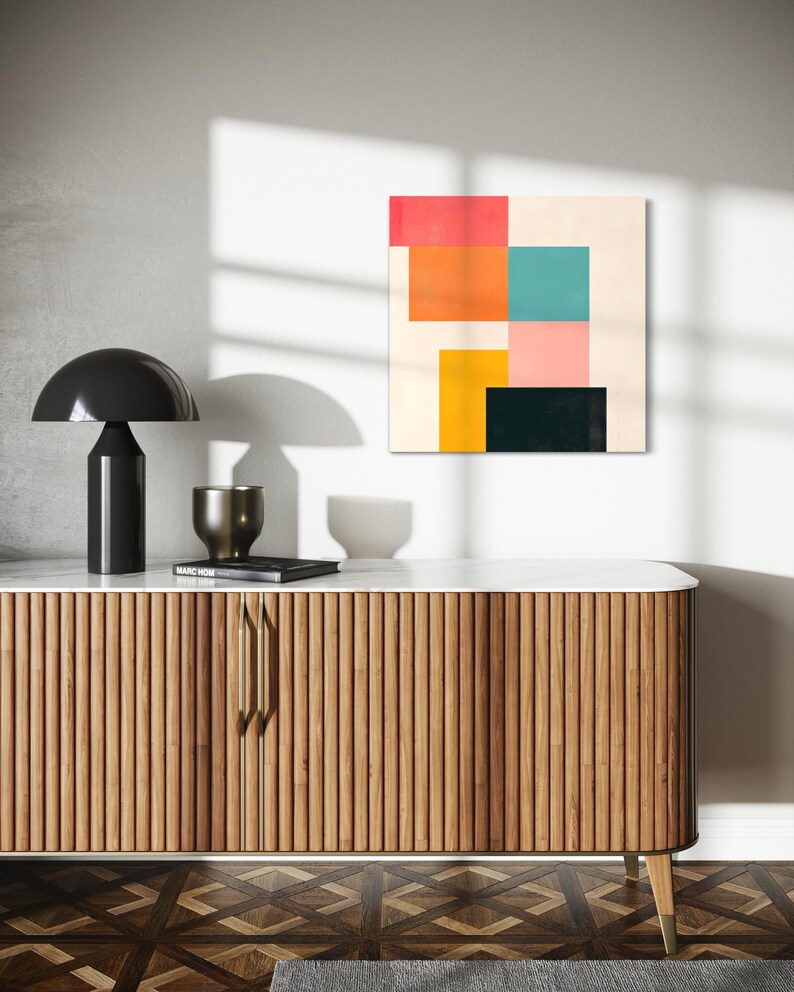 Puede incluir: Una impresi&oacute;n de arte abstracto moderno con formas geom&eacute;tricas en rosa, naranja, amarillo, turquesa y negro sobre un fondo crema. La impresi&oacute;n est&aacute; colgada en una pared blanca sobre un gabinete de madera con una tapa de m&aacute;rmol.