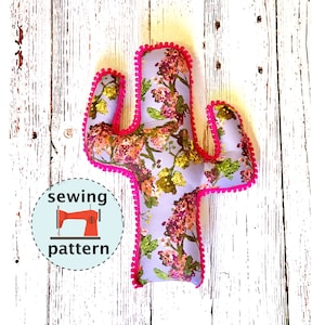 May include: A sewing pattern for a cactus pillow. The pillow is made of floral fabric with a pink pom-pom trim. The pattern is available for download.