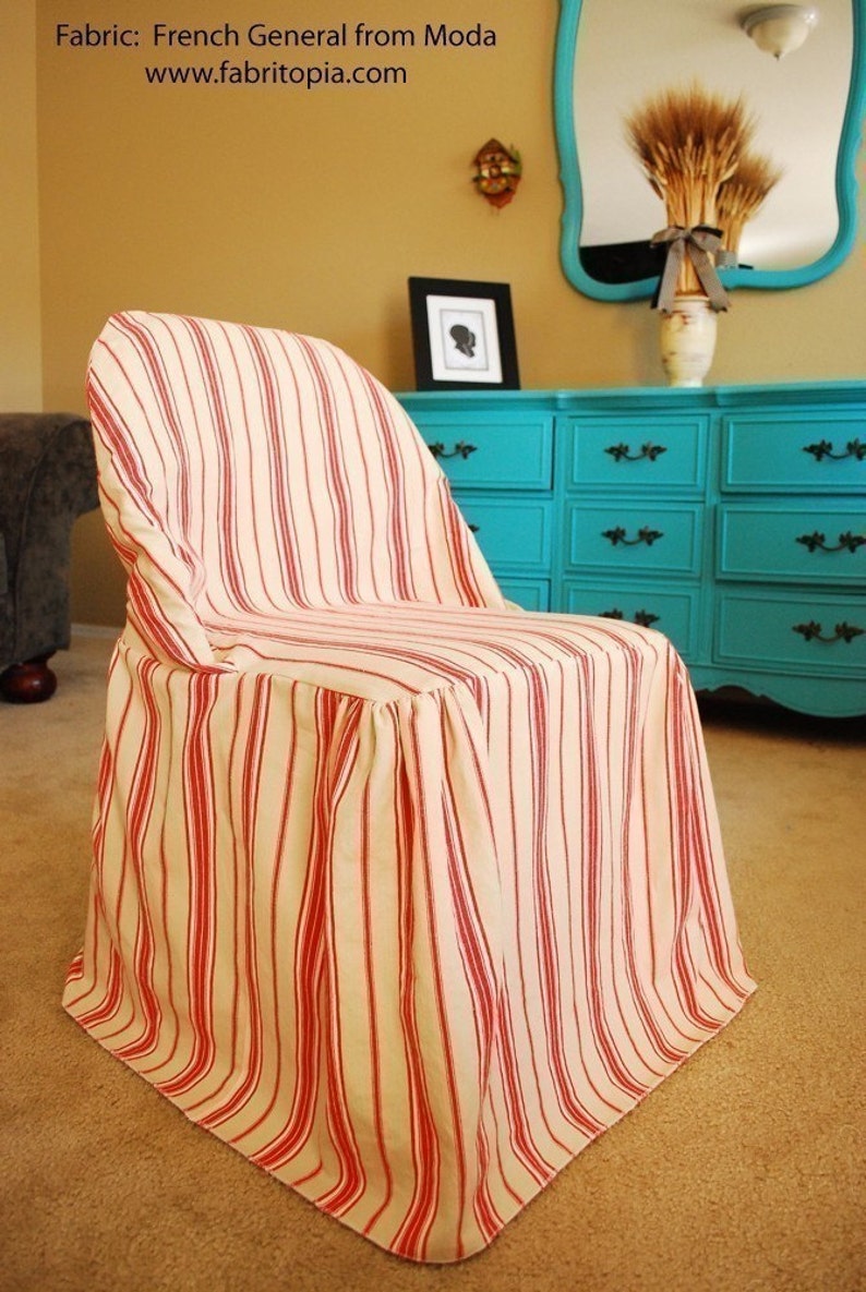 May include: A chair covered in fabric with vertical red stripes on a cream background. The fabric drapes over the chair, creating a skirted effect. The chair is in a room with a turquoise dresser and a mirror.