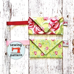 May include: Two fabric envelope style pouches with floral patterns. The top pouch is green and pink with larger floral designs. The bottom pouch is green with smaller floral designs. Both pouches have a pink or red ribbon attached.