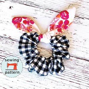 Pode incluir: Um scrunchie xadrez preto e branco com um laço branco e orelhas de coelho de tecido floral. O scrunchie está sobre um fundo de madeira branco. "padrão de costura" está escrito em um círculo com um ícone de máquina de costura.