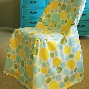 May include: A chair covered in fabric with a pattern of large yellow, green, and light blue circles on a white background. The chair is in front of a turquoise dresser.