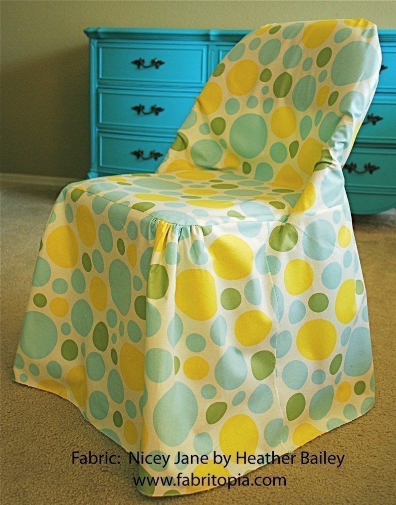 May include: A chair covered in fabric with a pattern of large yellow, green, and light blue circles on a white background. The chair is in front of a turquoise dresser.