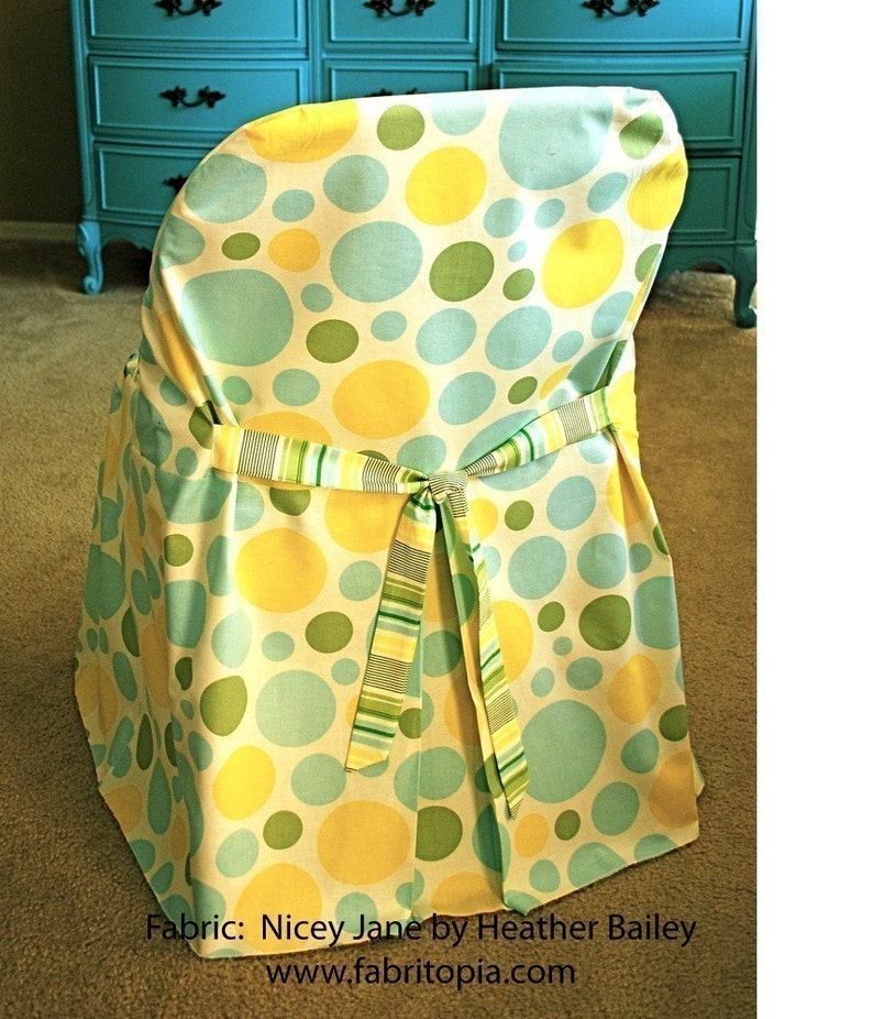 May include: Chair cover with a pattern of large yellow, green, and blue circles on a cream background. The cover is tied with a striped ribbon. The text "Fabric: Nicey Jane by Heather Bailey" is visible.