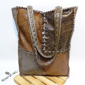 Puede incluir: Bolso tote de cuero hecho a mano en tonos marrón y gris. El bolso presenta un diseño de patchwork con costuras visibles y tachuelas metálicas decorativas. Las correas son de un marrón más claro con costuras decorativas.