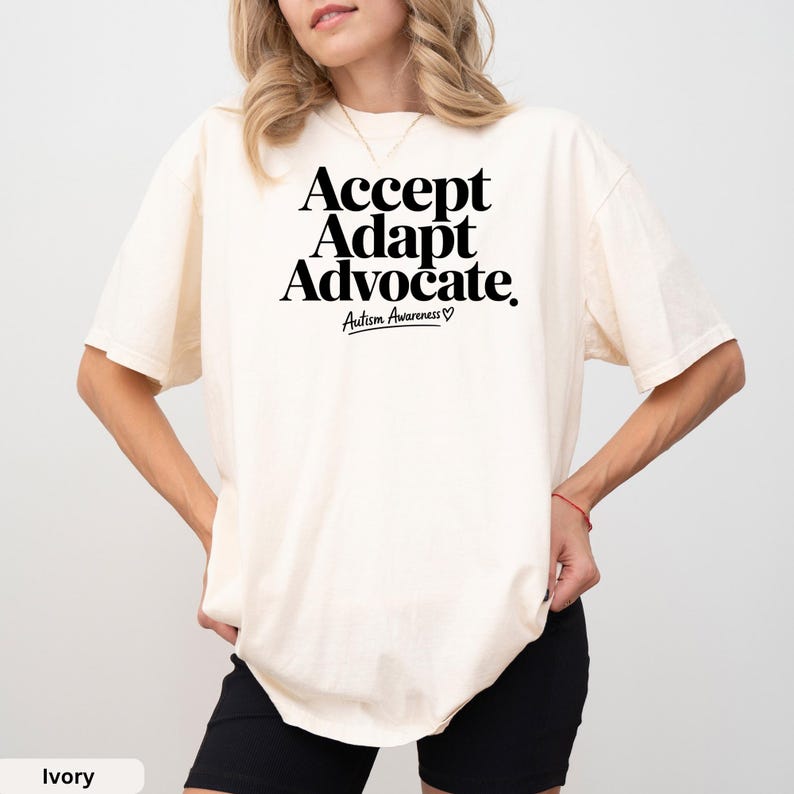 A woman wearing a white t-shirt with the text "Accept Adapt Advocate Autism Awareness" printed on it.