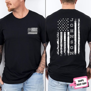 May include: Black crew neck t-shirt with a distressed white American flag graphic on the front and back. The back of the shirt features the name "JOHNSON" vertically. A small flag is on the front left chest.