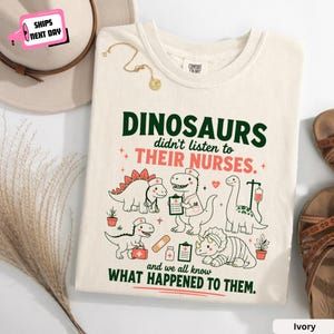 Puede incluir: Una camiseta de color marfil con un gráfico de cuatro dinosaurios vestidos como profesionales médicos y el texto "DINOSAURS didn't listen to THEIR NURSES. and we all know WHAT HAPPENED TO THEM." El diseño incluye iconos médicos como un portapapeles, una bolsa de suero y una tirita.