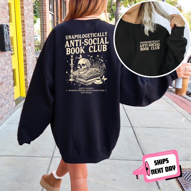 A person wearing a black sweatshirt with text and an illustration on the back, walking on a sidewalk.